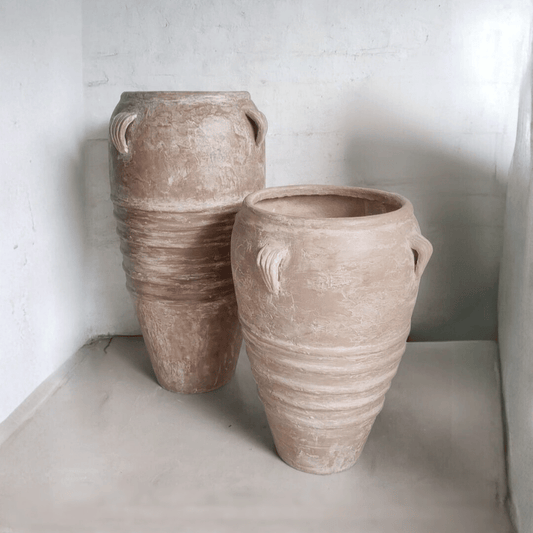 Two terracotta looking fiberglass pots on a light surface with a white wall background