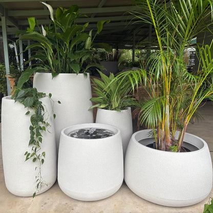 The Florastyle By Hingham Full Bios Set with One Bios Medium Water Feature features five large, modern white planters displaying lush green plants and a water feature on a concrete floor in a covered outdoor space.