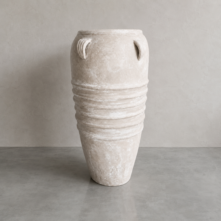 The Athens Organic Fiberglass Pot from Florastyle By Hingham's Earth Range, with horizontal ridges and loop handles inspired by ancient Greek pottery, stands on a smooth gray surface against a light beige wall.