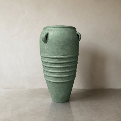 The Athens Organic Fiberglass Pot - Earth Range by Florastyle By Hingham is a tall, green pot inspired by ancient Greek pottery, featuring two small top handles and four midsection ridges, shown on a smooth floor against a plain beige wall.