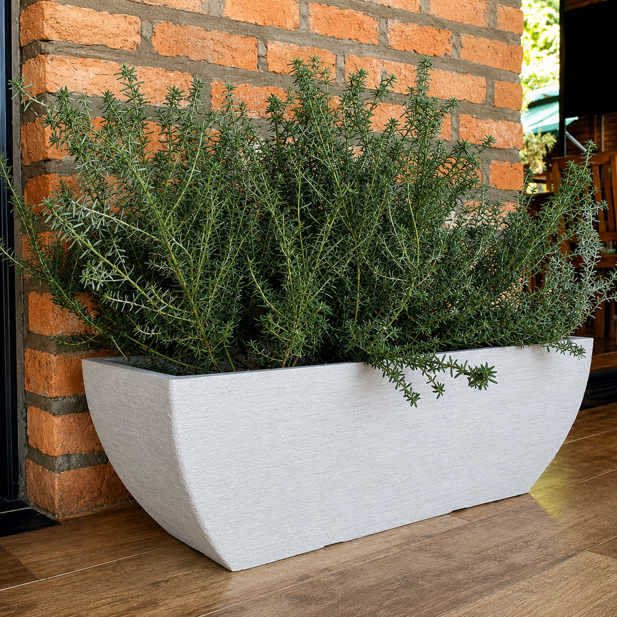 A Japi Modern Square Window Box by Florastyle By Hingham, filled with dense green rosemary, sits on a wooden floor in front of a brick wall.