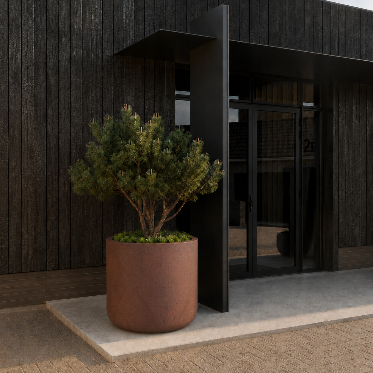 A Nativa Japi Planter by Florastyle By Hingham, featuring smart drainage and controlled lighting and irrigation options, displays lush green foliage on a concrete slab outside a modern building with dark wood paneling and glass doors.