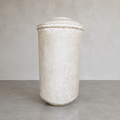 The Damascus Organic Fiberglass Pot - Earth Range by Florastyle By Hingham is a large, off-white cylindrical planter with a domed lid, placed on a gray surface against a light textured wall—perfect for modern interiors.