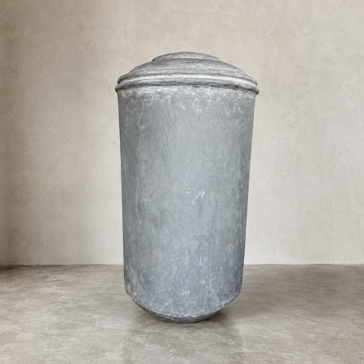 The Damascus Organic Fiberglass Pot - Earth Range by Florastyle By Hingham, featuring a domed lid and weathered finish, stands on a gray concrete floor against a light beige textured wall.