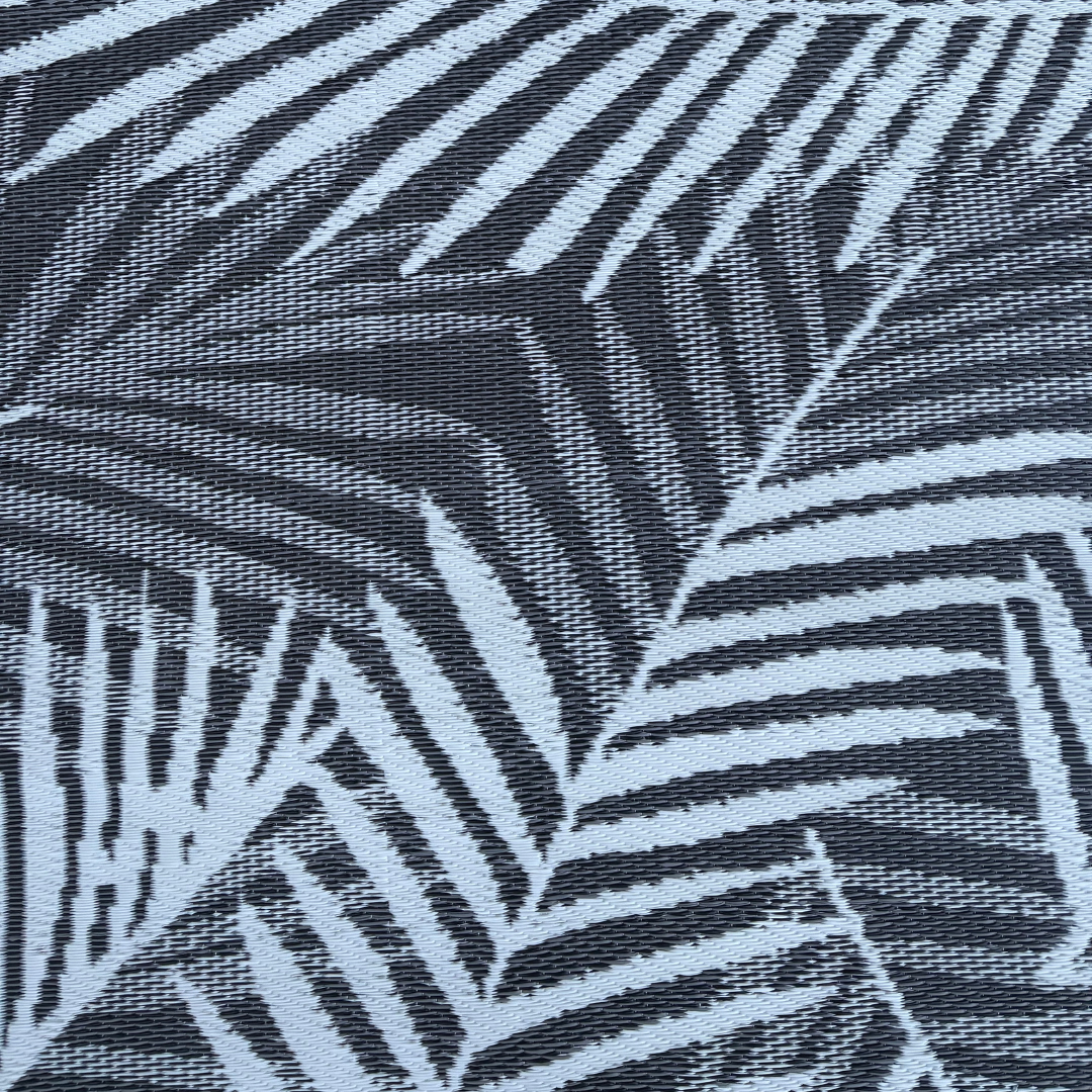Close-up of the Florastyle By Hingham Medium Hanoi Outdoor Reversible Mat, made from lightweight, double-woven, water-resistant fabric with a bold modern pattern of overlapping palm leaves in light blue and dark gray.