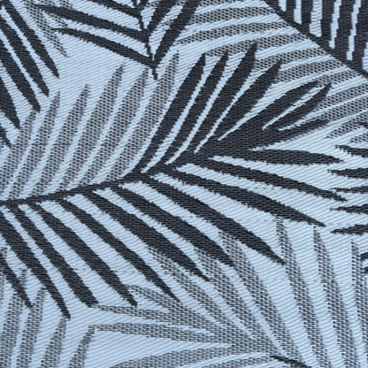 Black palm leaf silhouettes overlap on a light blue background, creating a bold, tropical look. The Medium Hanoi Outdoor Reversible Mat by Florastyle By Hingham is lightweight, double woven, and water resistant for comfort and durability.