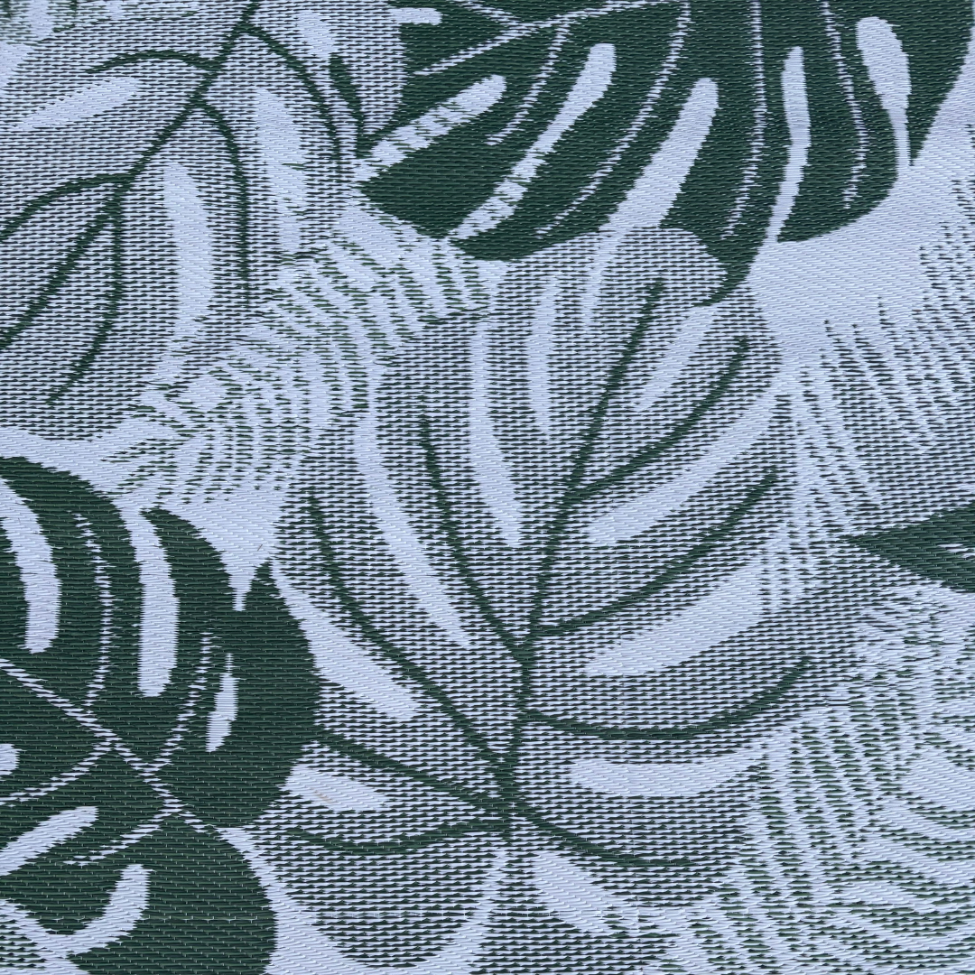 Close-up of Florastyle By Hingham’s Medium Lima Outdoor Reversible Mat, featuring lightweight, double-woven fabric with a large green monstera and fern motif on a light background. Water-resistant design delivers a textured, tropical look.