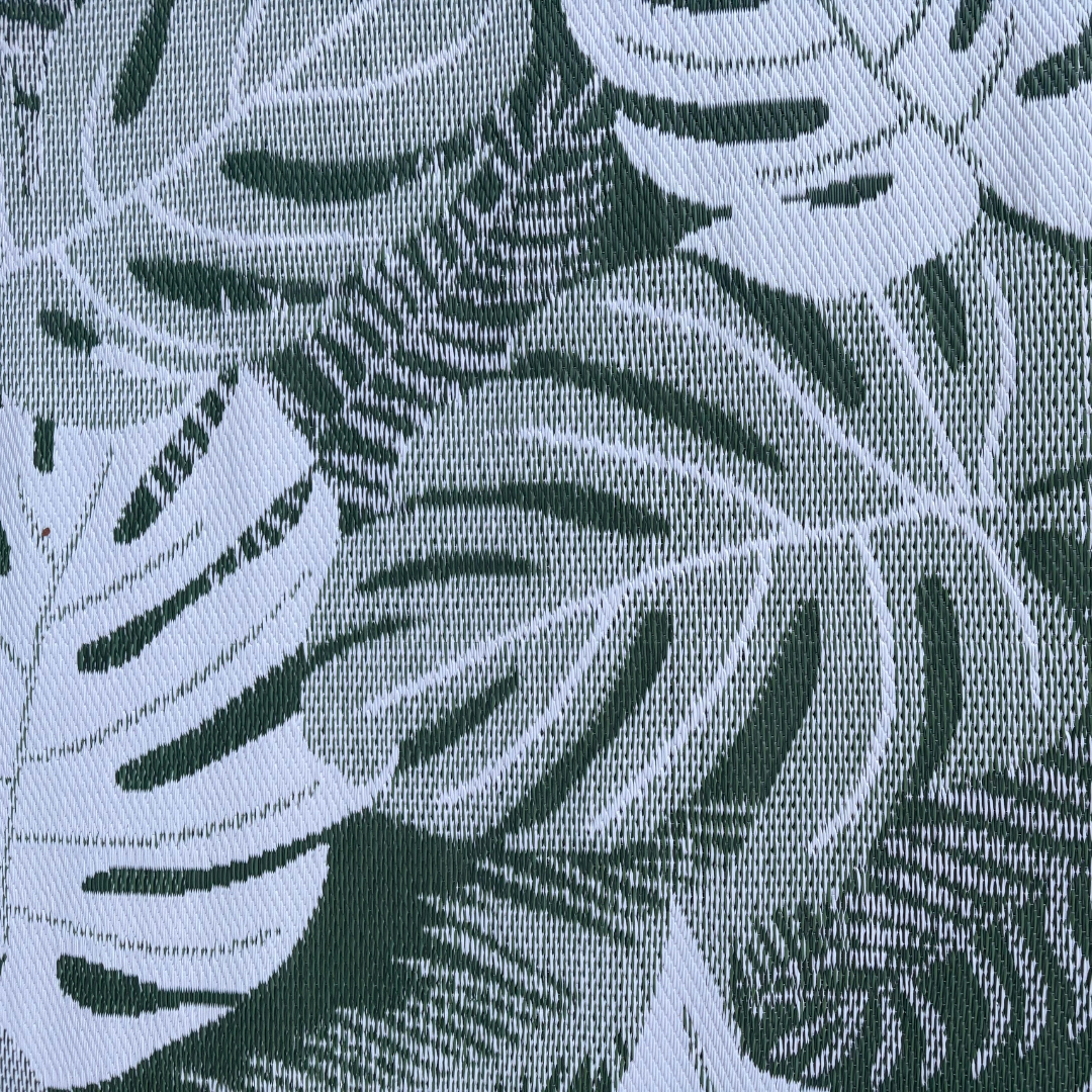 Close-up of the Florastyle By Hingham Medium Lima Outdoor Reversible Mat, showcasing its lightweight, double woven texture and large green and white tropical leaf pattern. Water-resistant for versatile outdoor use.