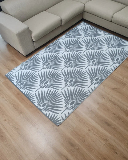 The Florastyle By Hingham Medium Mumbai Outdoor Reversible Mat, a lightweight gray and white rug with a palm leaf pattern, is placed on a light wood floor next to a beige sectional sofa in this modern living room.