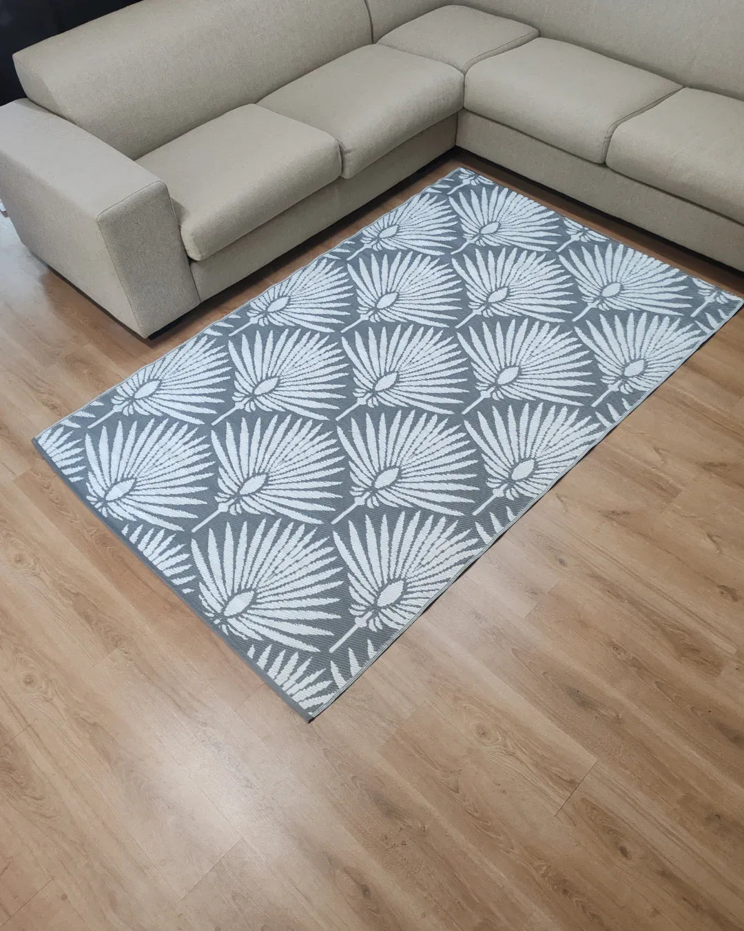 A Medium Mumbai Outdoor Reversible Mat by Florastyle By Hingham, featuring a lightweight double-woven design and water resistance, is placed on a light wood floor next to a beige L-shaped sofa.