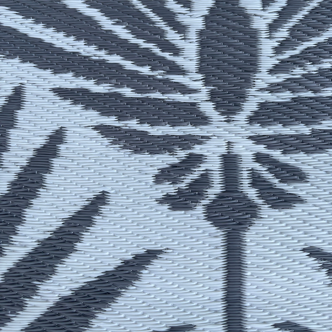 Close-up of the Florastyle By Hingham Medium Mumbai Outdoor Reversible Mat, showcasing its lightweight, double woven plastic design with a black and gray abstract leaf pattern on a light gray background. Water resistant.