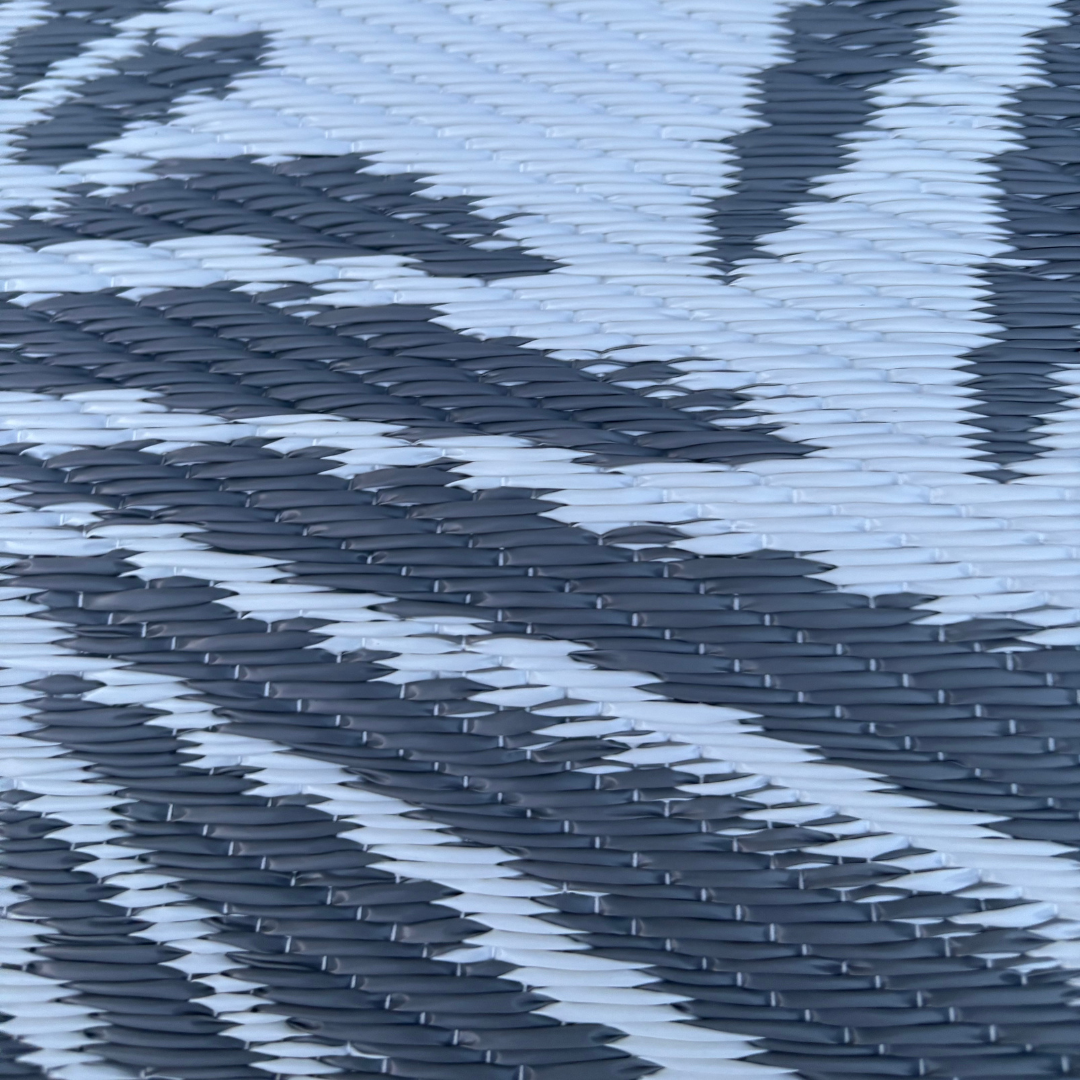 Close-up of the Florastyle By Hingham Medium Mumbai Outdoor Reversible Mat, featuring a lightweight, double woven, water-resistant surface with overlapping gray and white abstract shapes resembling scales or feathers.