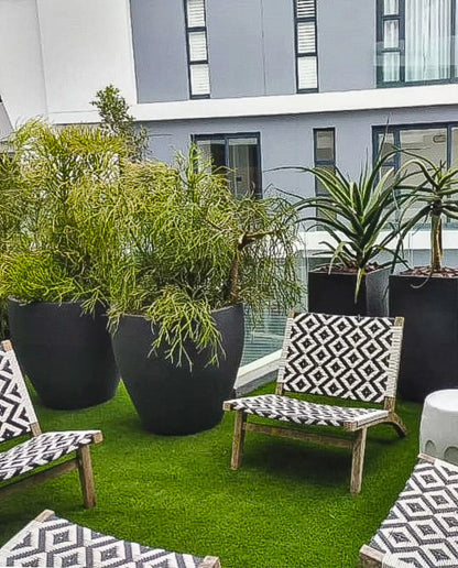 A large Lead coloured, rustic ellipse japi planteroutdoor planter, placed on a green lawn with a chair and table set in the foreground.