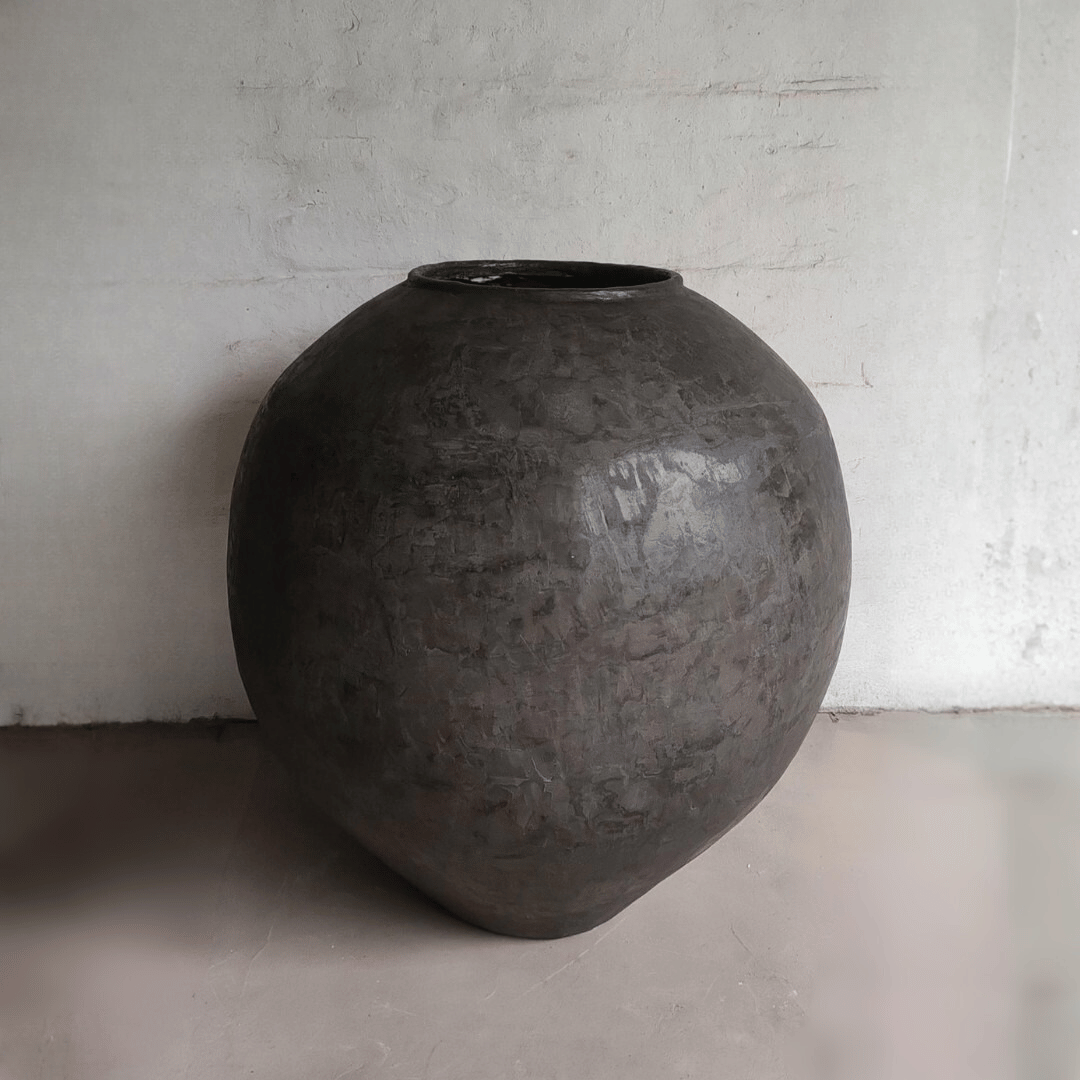 Large black textured vase on a light gray floor with a white wall background