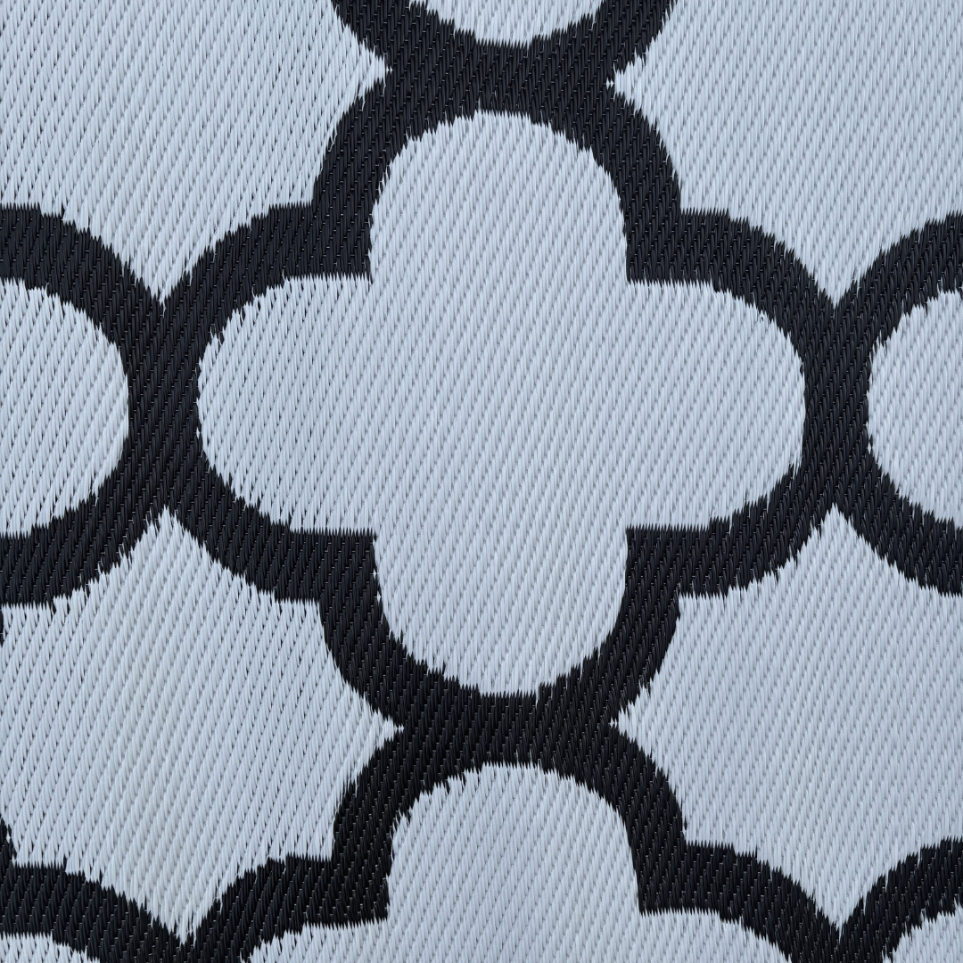 Close-up of Florastyle By Hingham’s Medium Tripoli Outdoor Reversible Mat, featuring lightweight double woven fabric with black quatrefoil-like geometric patterns on a light gray water-resistant surface with diagonal textured accents.