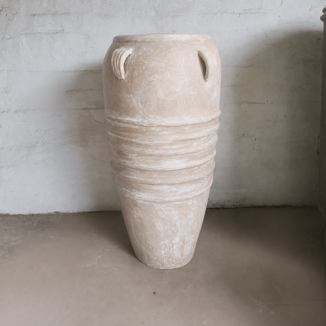 The Athens Organic Fiberglass Pot - Earth Range by Florastyle By Hingham features a tall, beige design inspired by ancient Greek pottery, with a narrow base, rounded top, and four small handles—perfect against a textured wall on any smooth floor.