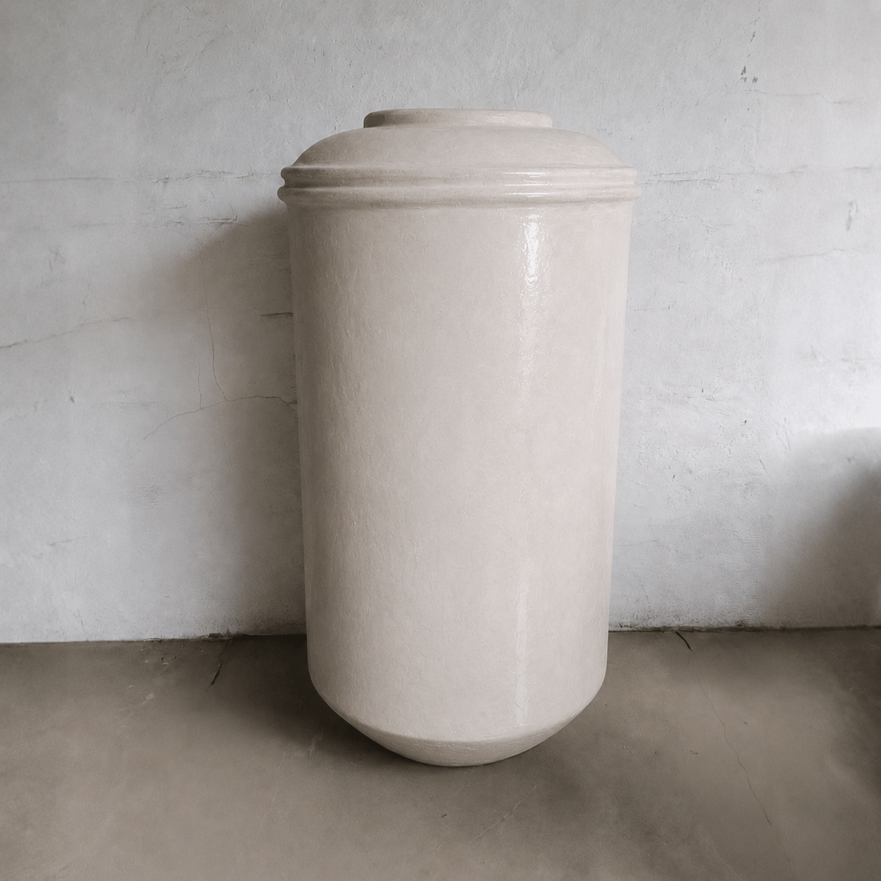 The Damascus Organic Fiberglass Pot - Earth Range by Florastyle By Hingham, a tall cylindrical planter in smooth, off-white finish, stands against a plain wall and concrete floor in a minimalist setting.