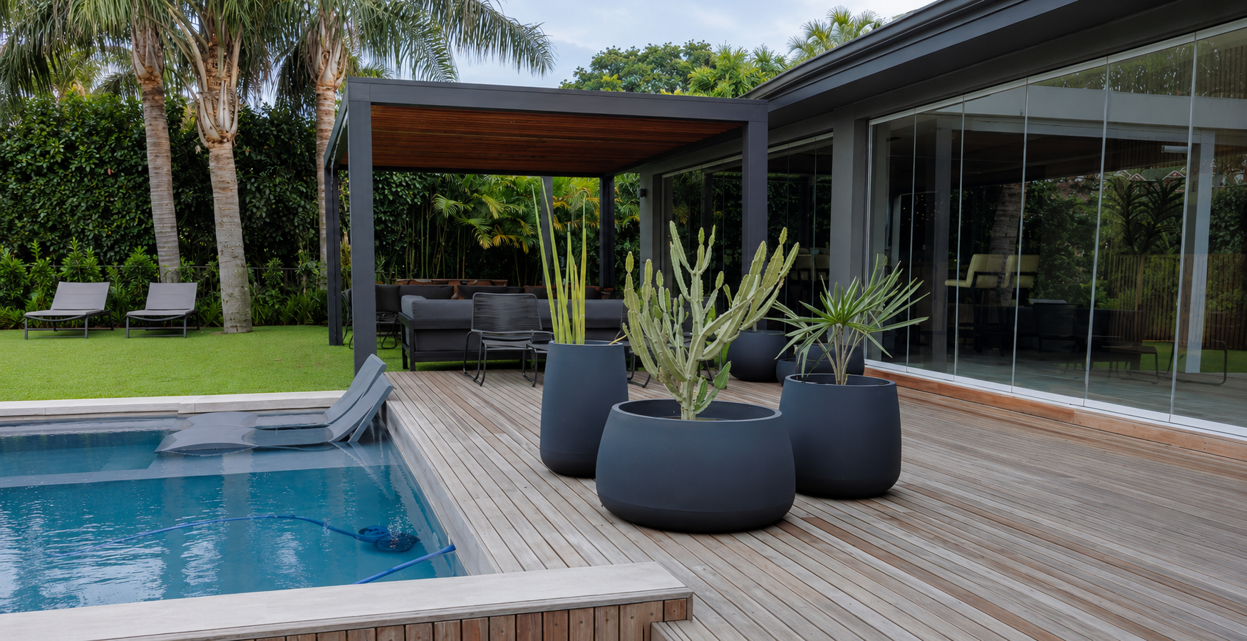Modern outdoor setting with a pool, wooden deck, and potted plants. Japi Bios original set Planters.