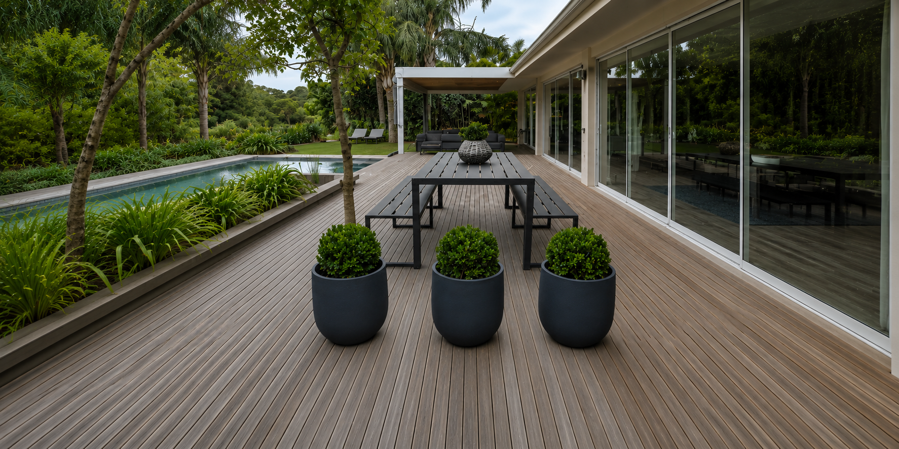 Modern outdoor patio with wooden deck, pool, and potted plants. Japi Rustic Cask Lead planters.