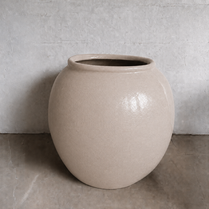 The Delphi Organic Fiberglass Pot - Earth Range by Florastyle By Hingham, large and round with a wide opening, rests on a smooth concrete floor against a light gray textured wall.