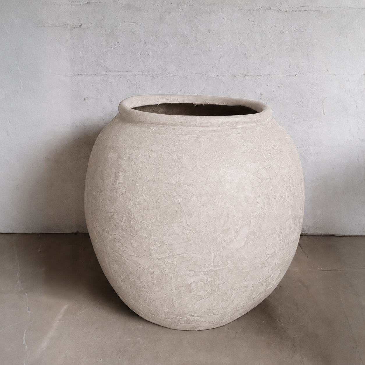 The Delphi Organic Fiberglass Pot - Earth Range by Florastyle By Hingham sits on a smooth floor against a textured, light gray wall, its wide opening and beige finish offering timeless elegance in classic planter design.