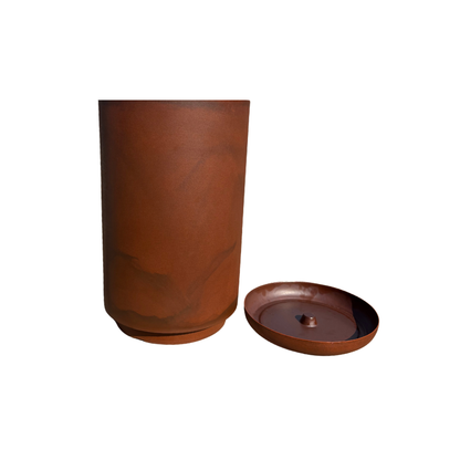 A tall, cylindrical brown Match Cylinder Japi Planter With Saucer by Florastyle By Hingham stands on a white background, with its matching round lid featuring a small raised center placed beside it.