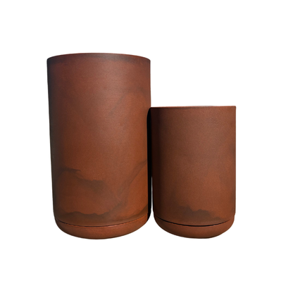 The Match Cylinder Japi Planter With Saucer by Florastyle By Hingham features two rust-colored, cylindrical planters of varying heights with a smooth matte finish and subtle color variations, creating a stylish, contemporary look against a white background.