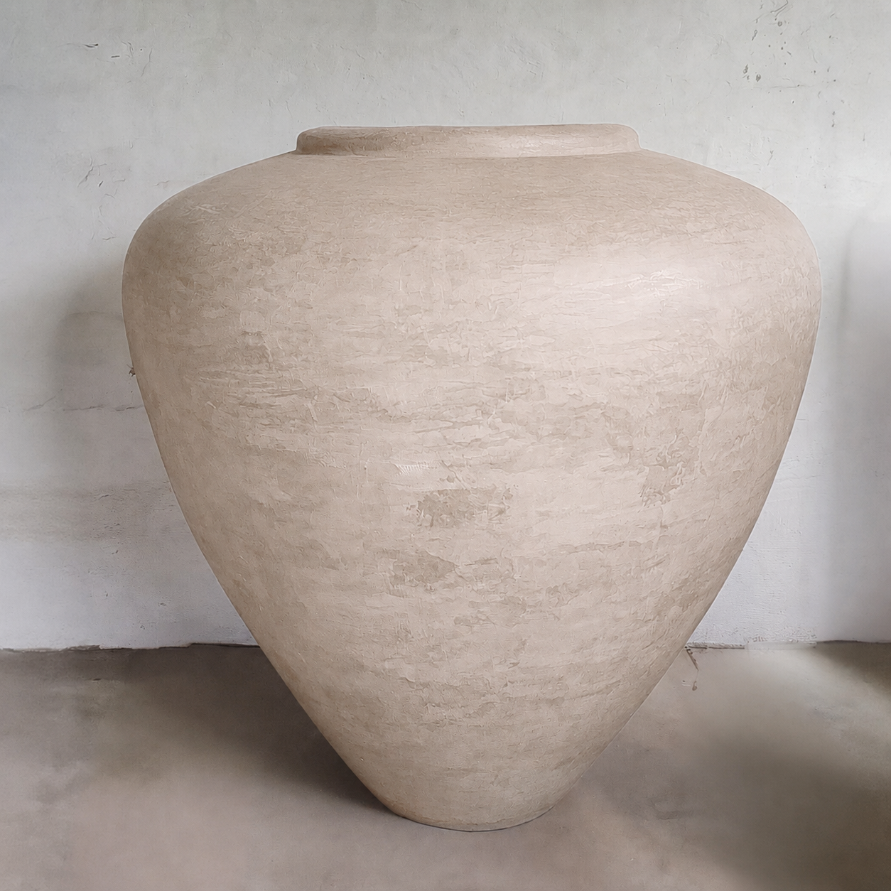 The Mykonos Organic Fiberglass Pot - Earth Range by Florastyle By Hingham features a large, textured beige finish with a wide body and narrow base—ideal as sculptural décor against a light wall on a smooth floor.