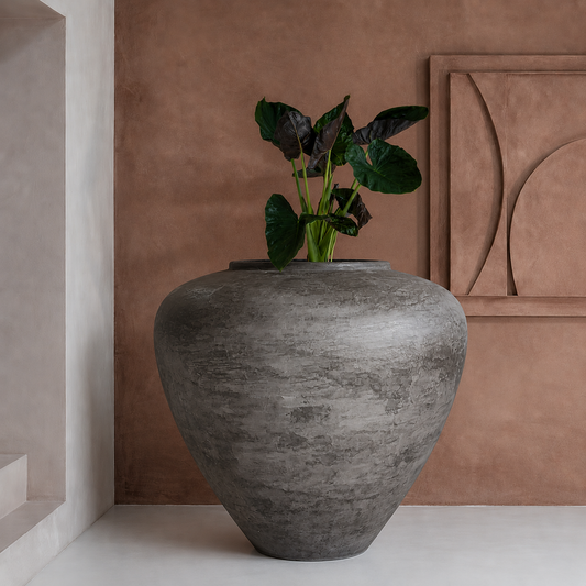 The Mykonos Organic Fiberglass Pot - Earth Range by Florastyle By Hingham, featuring a green leafy plant, stands out against a brown textured wall with geometric art and a white alcove, bringing sculptural minimalism to modern interiors.