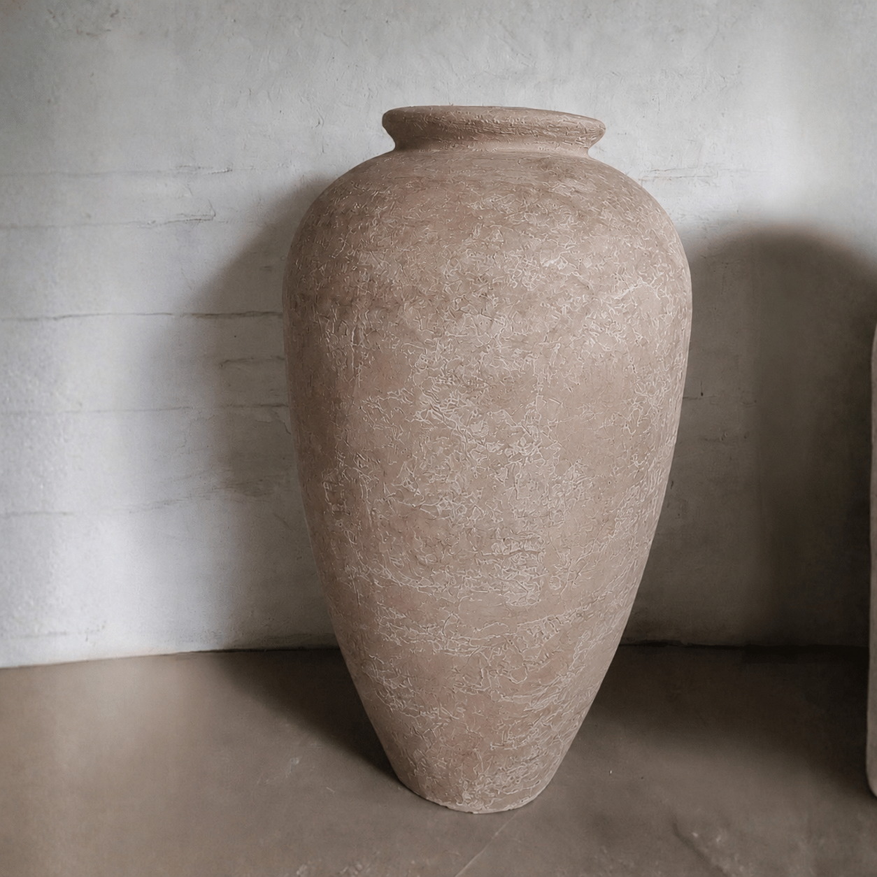 A large, beige Rhodes Organic Fiberglass Pot from Florastyle By Hingham’s Earth Range with a wide mouth stands on a smooth floor against a lightly textured, pale wall.