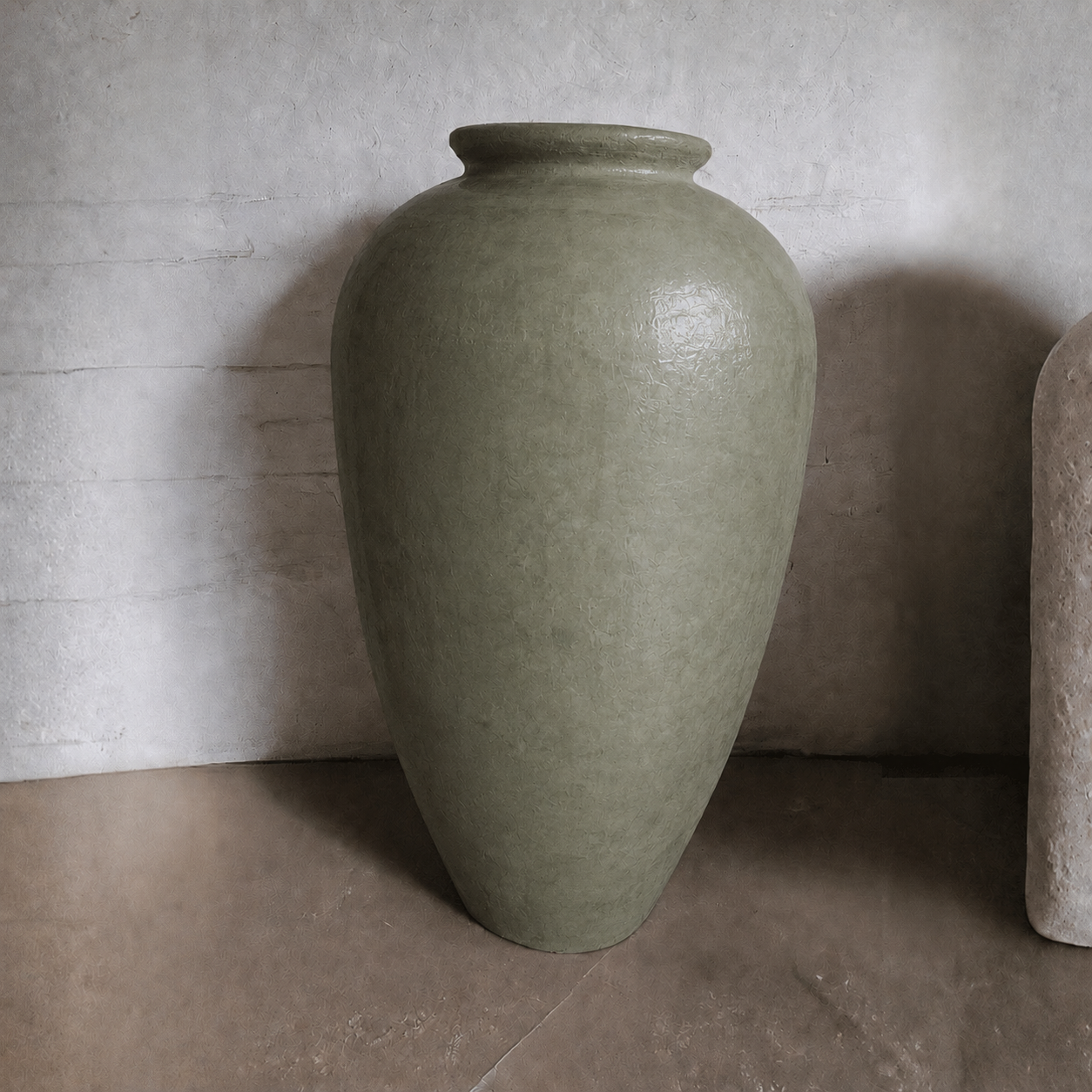 A large, olive-green Rhodes Organic Fiberglass Pot from Florastyle By Hingham sits on a stone floor against a textured, light gray wall.