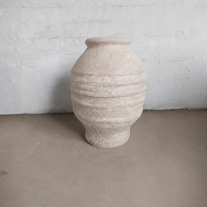 The Sparta Organic Fiberglass Pot - Earth Range by Florastyle By Hingham features textured beige horizontal ridges, standing on a light brown floor with a white wall—an ideal choice for organic modern decor.