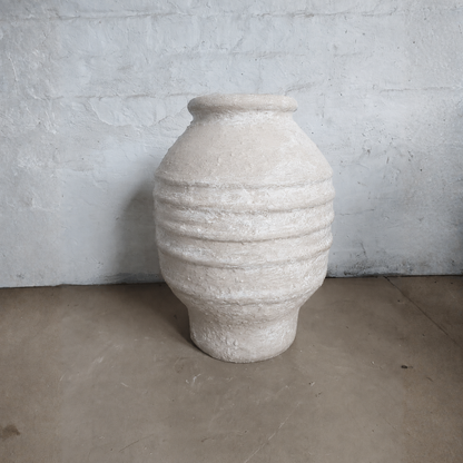 The Sparta Organic Fiberglass Pot - Earth Range by Florastyle By Hingham is a large, textured beige planter with horizontal ridges—an ideal lightweight accent for organic modern decor on a bare concrete floor.